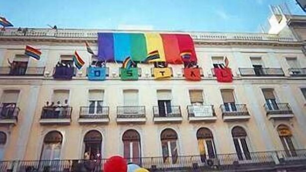 Fachada de edificio con balcones y una bandera arcoíris.