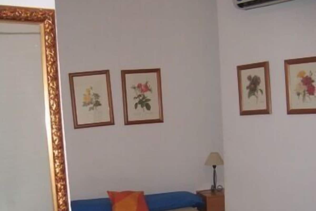 Un dormitorio con cama, mesita de noche, lámpara y cuadros con motivos florales en la pared.