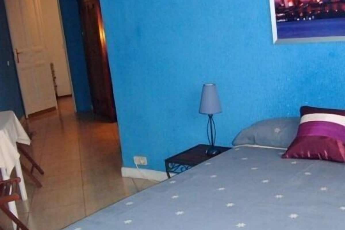 Un dormitorio con cama, mesita de noche, lámpara y vistas a un edificio de arquitectura rosa.