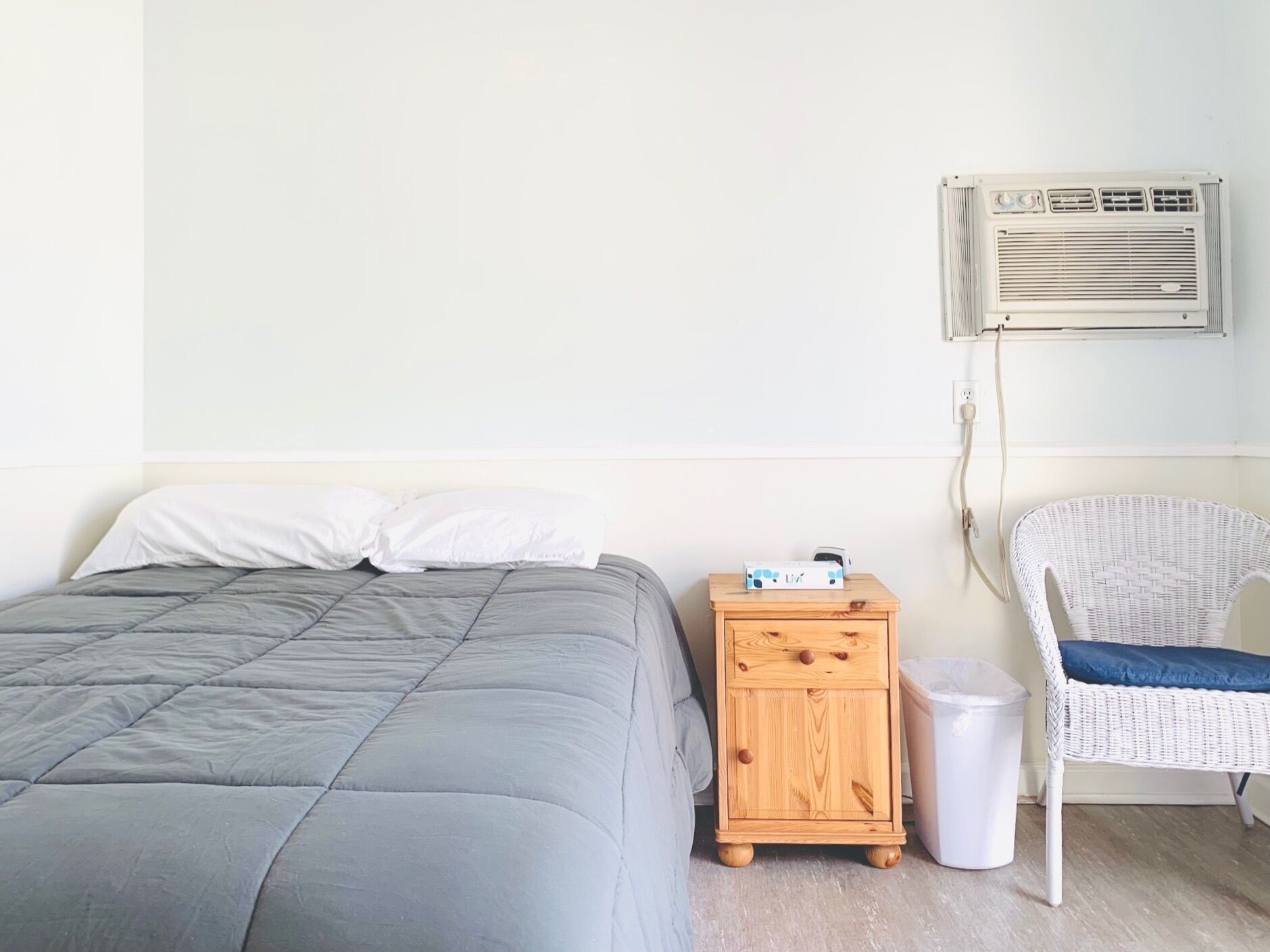 Un dormitorio con una cama, una mesita de noche, una silla y un equipo de aire acondicionado.