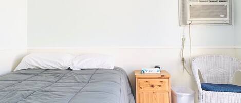 Un dormitorio con una cama, una mesita de noche, una silla y un equipo de aire acondicionado.