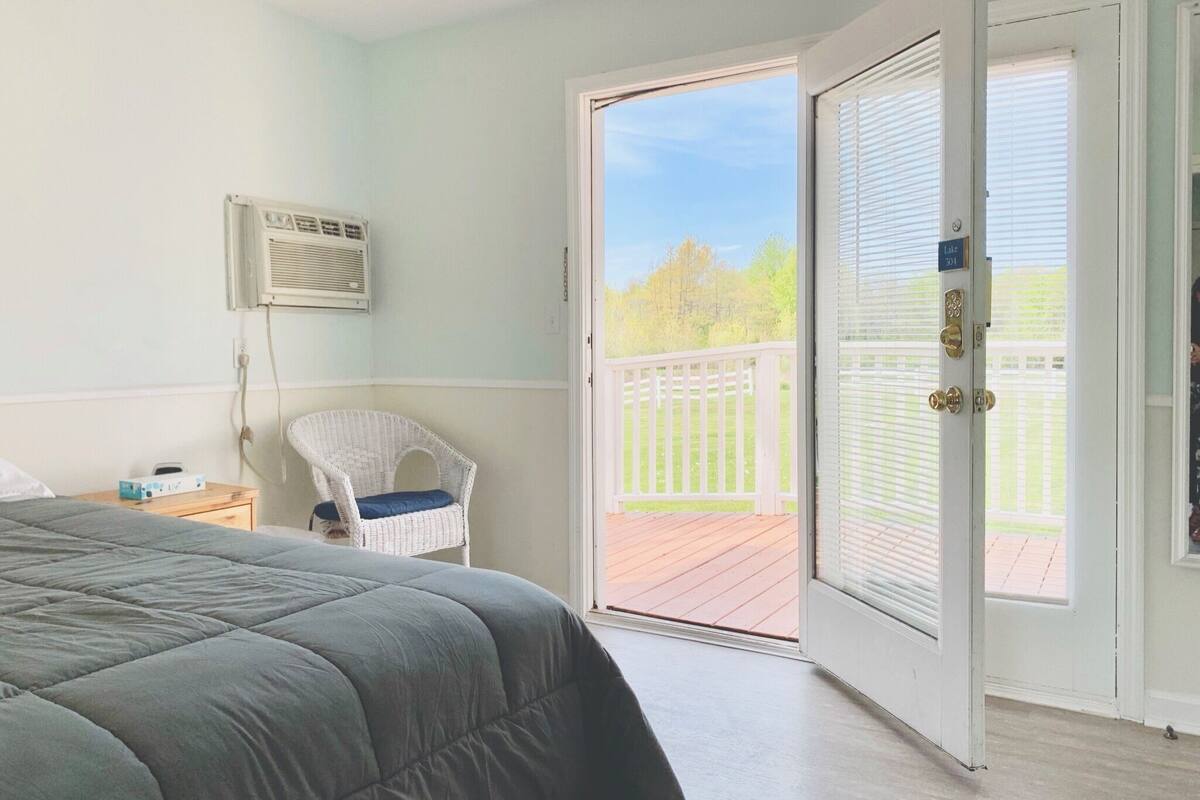 A bedroom with a bed, a chair, a nightstand, a window, and an open door to a balcony.