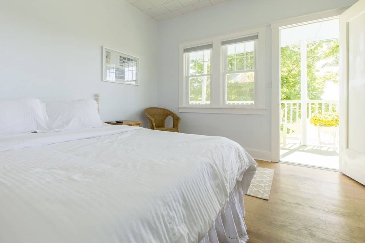 A bedroom with a large bed, a chair, a window, and a door leading to a balcony.