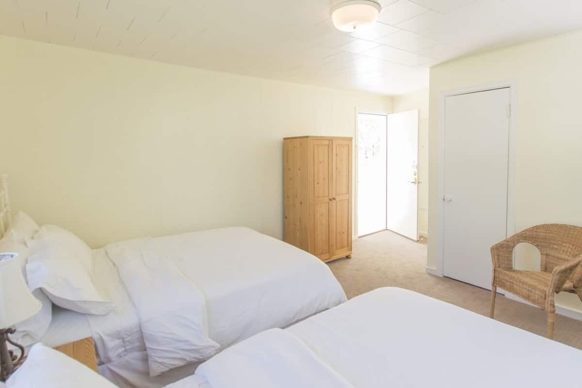 A bedroom with two beds, a wooden wardrobe, a wicker chair, and a white door.