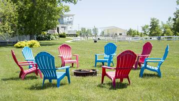 Un espace extérieur verdoyant, agrémenté de plusieurs fauteuils Adirondack aux couleurs vives, disposés autour d’un foyer central.