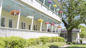 A two-story house with a white picket fence, a covered porch with hanging flower baskets, and a large tree in the front yard. - Sun N Sand Resort (South Haven)