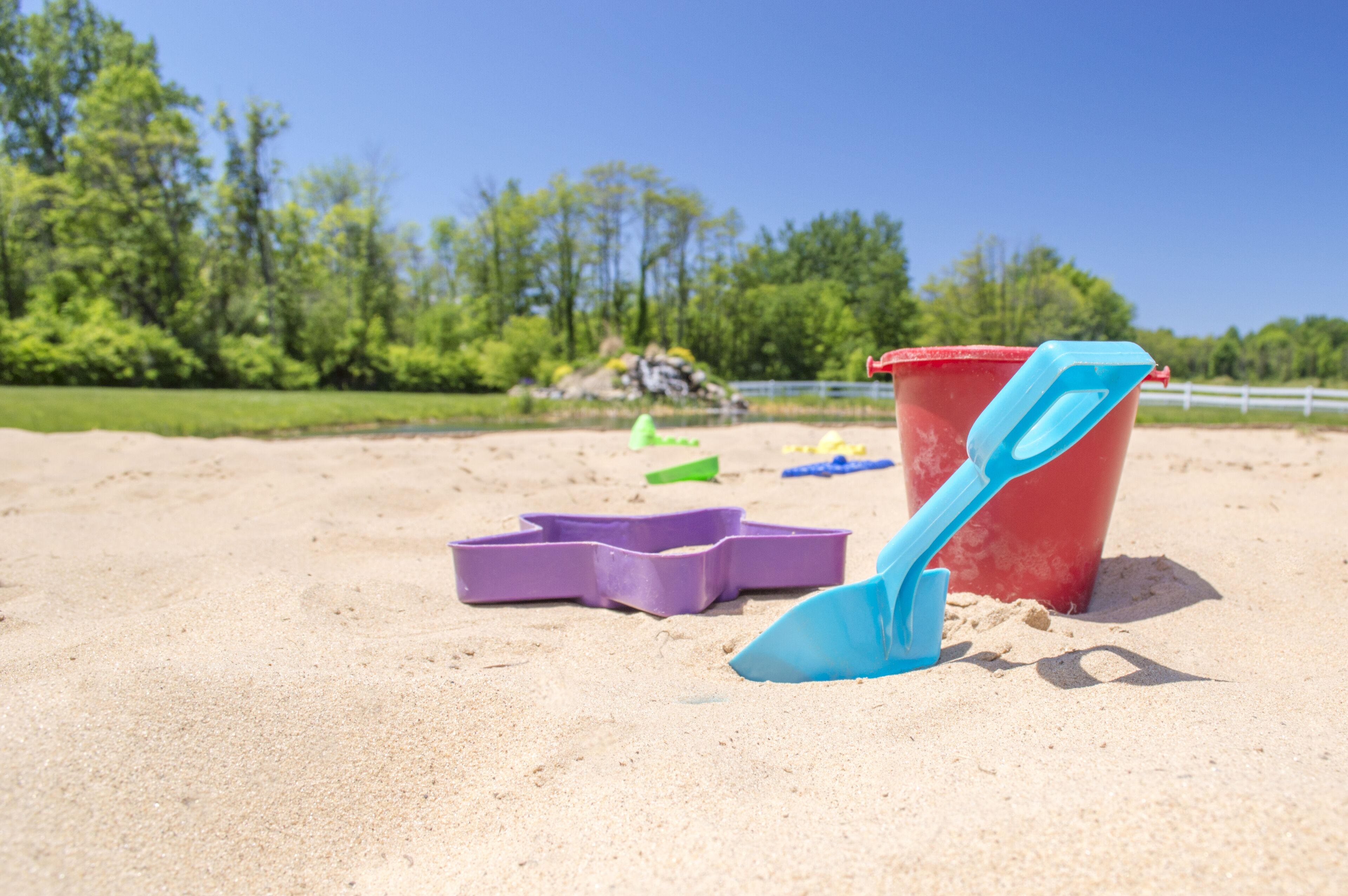 En strandscene med sand, en rød spand og en blå skovl.