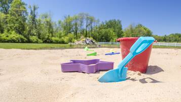 Une scène de plage avec du sable, un seau rouge et une pelle bleue.