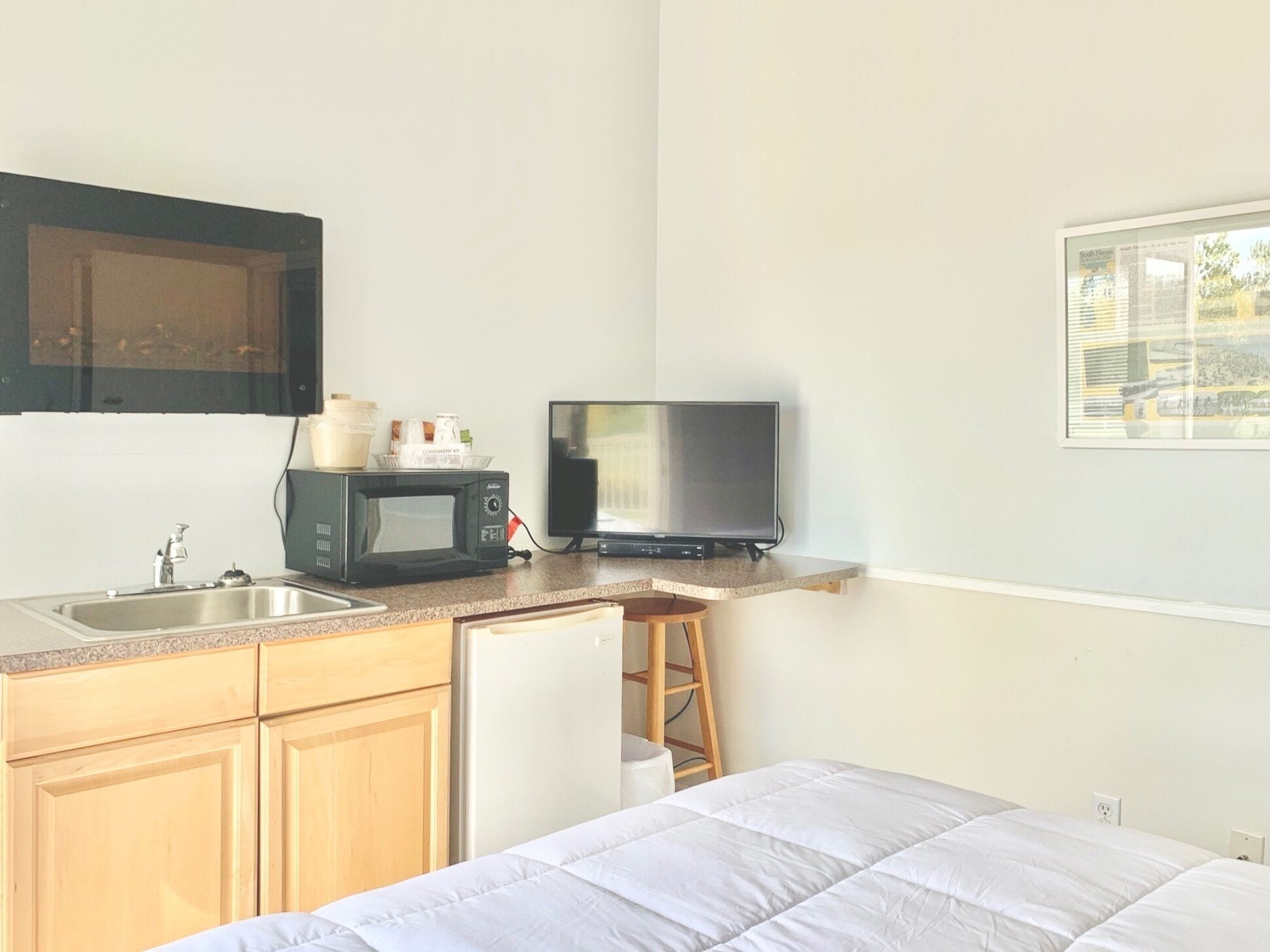 Una kitchenette compacta con microondas, pileta y heladera pequeña. Un televisor está montado en la pared sobre la mesada.