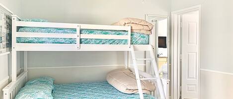 Una cama individual superpuesta con escalera, una mesita de noche pequeña y una ventana.