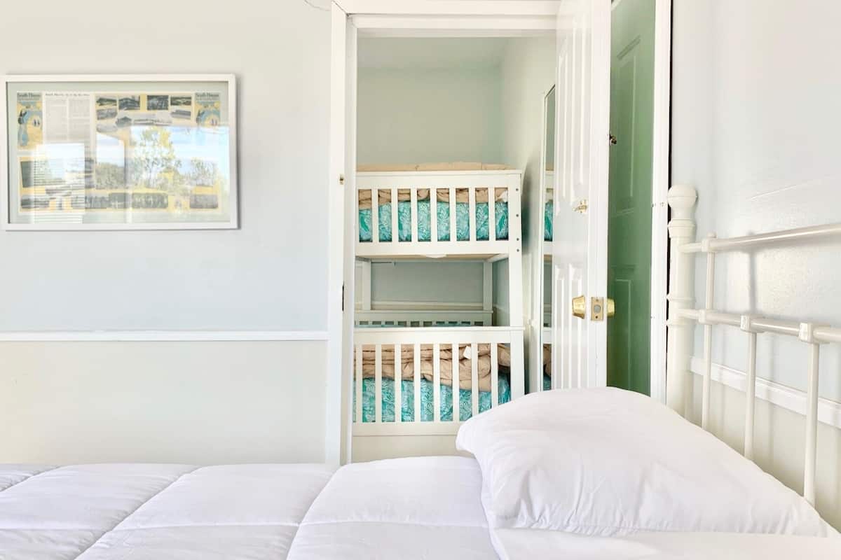 A room with a bed, a crib, and a door leading to a green hallway.