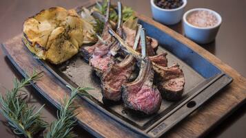 A wooden serving board with grilled lamb chops, roasted potatoes, and rosemary sprigs.