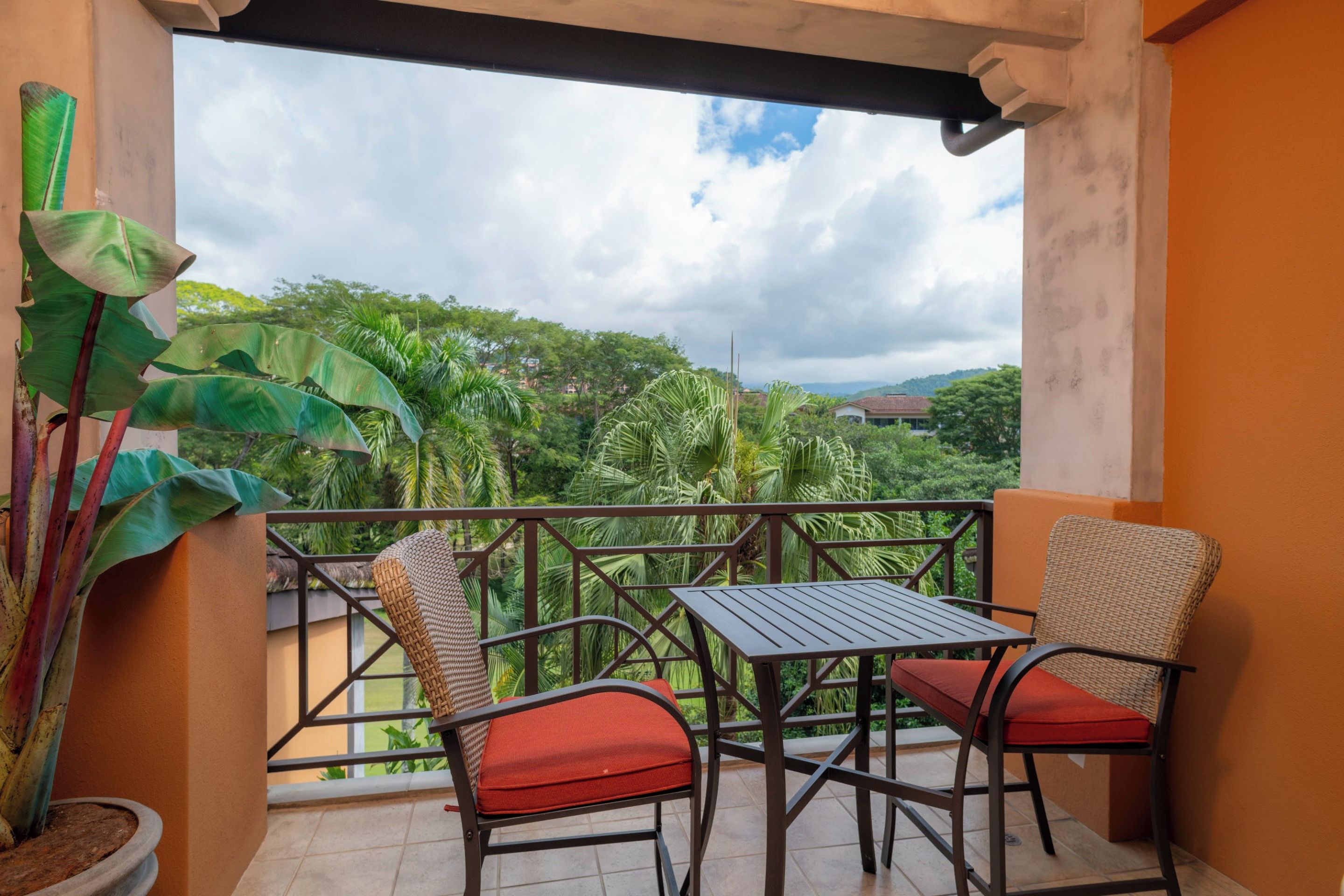 A balcony with a table and chairs, a potted plant, and a view of a green landscape.