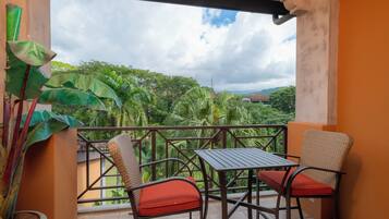 A balcony with a table and chairs, a potted plant, and a view of a green landscape.