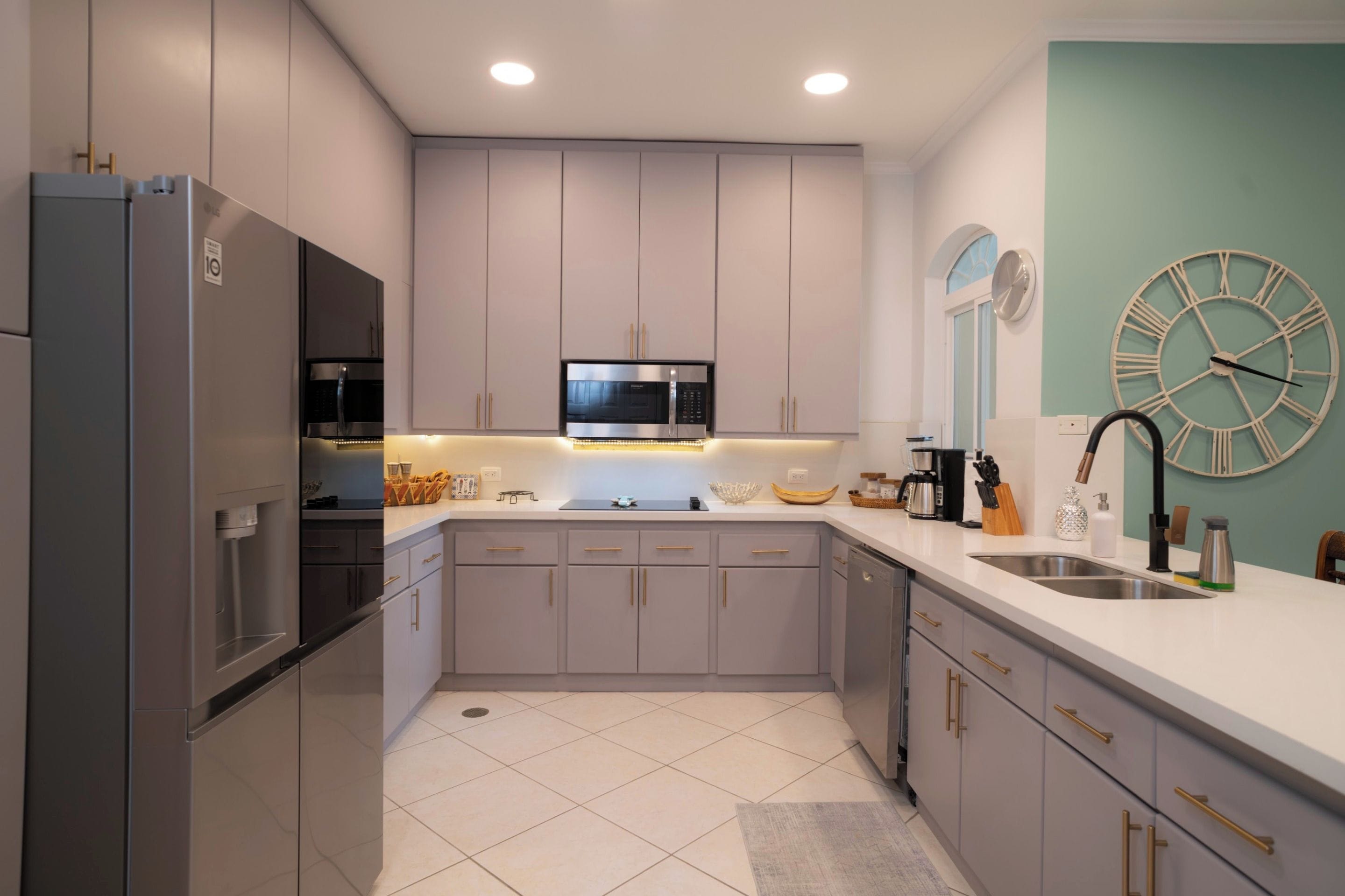 A modern kitchen with stainless steel appliances, a microwave, and a clock on the wall.