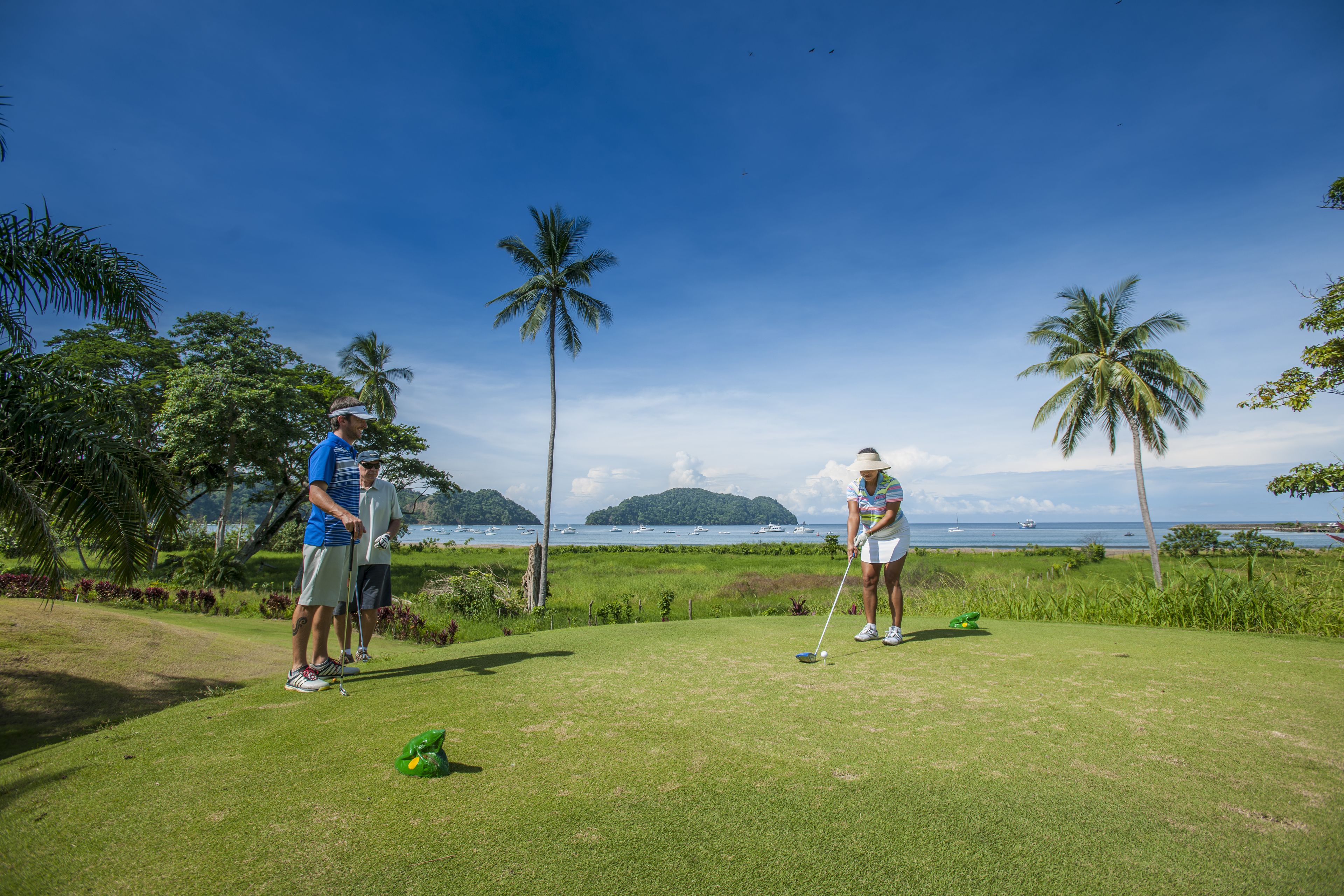 Un terrain de golf avec deux joueurs, des palmiers et une vue sur l’océan.