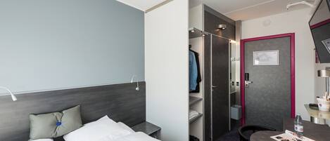 A hotel room with a bed, a desk, a chair, a wardrobe, and a bathroom.