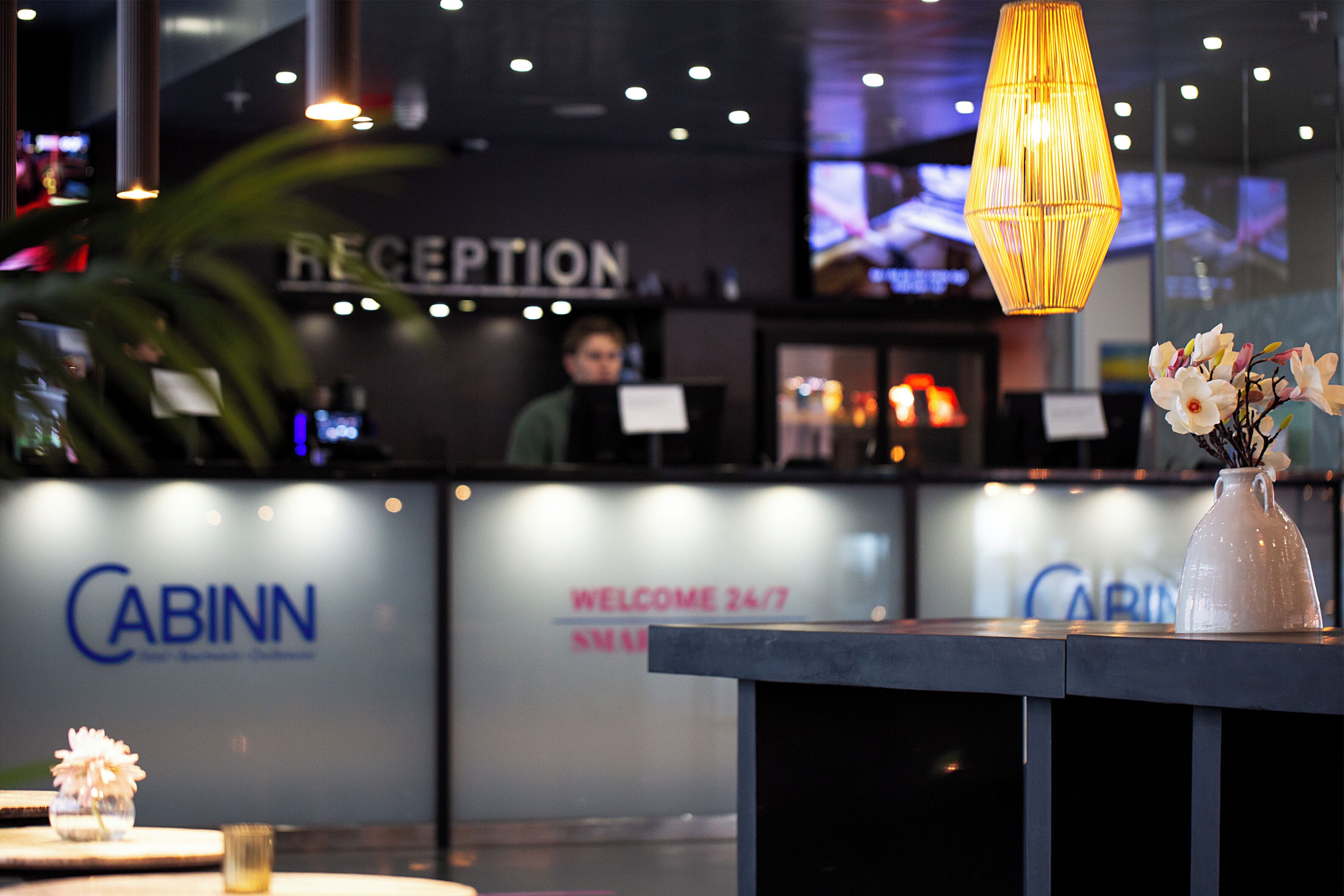 Et receptionsområde med et skilt der siger 'RECEPTION', et skilt der siger 'CABINN' og en meddelelse der siger 'VELKOMMEN 24/7'.