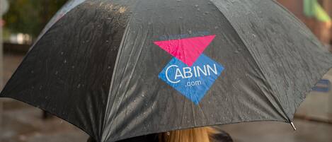A person holding a black umbrella with a logo, standing in a rainy outdoor setting.