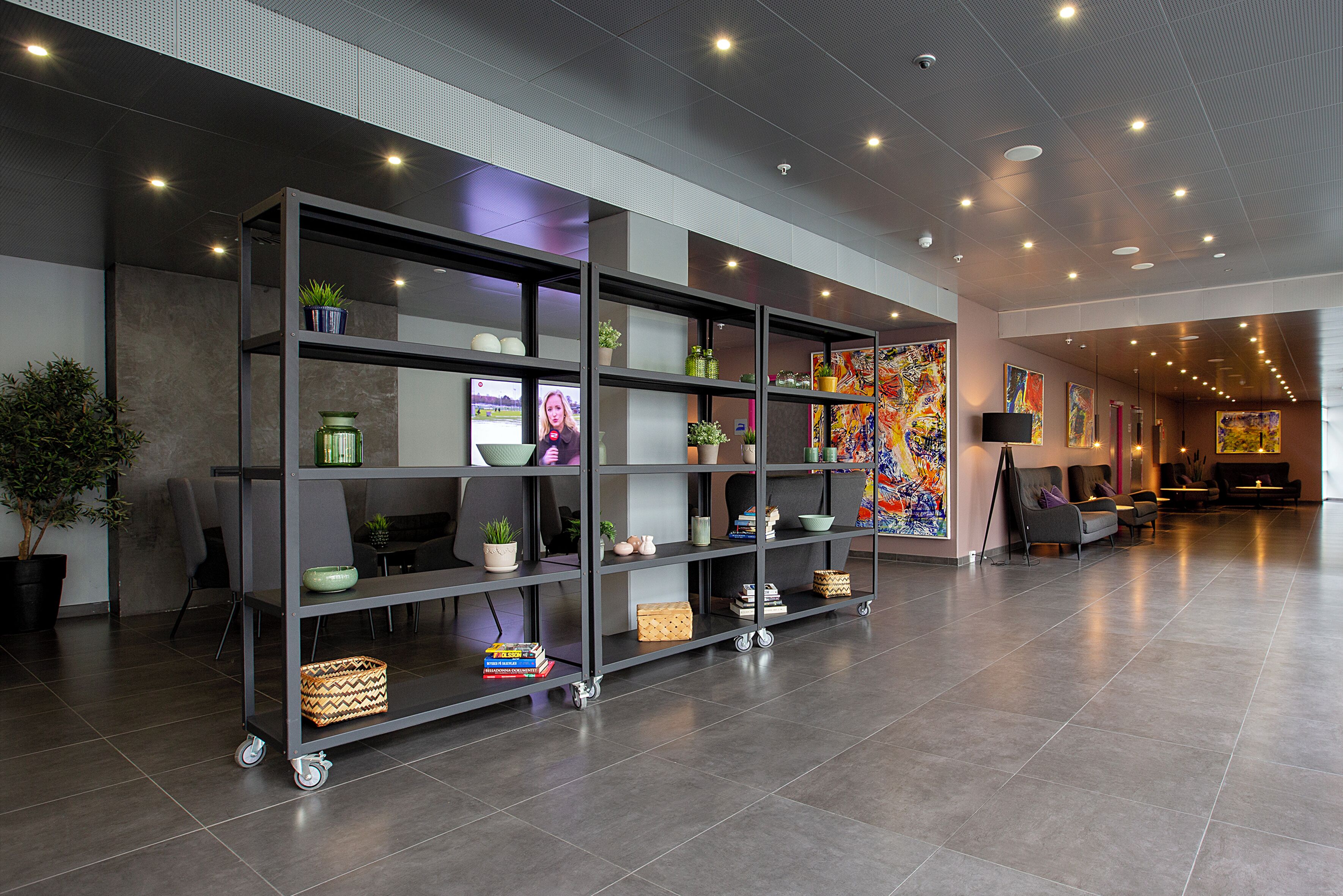A modern lobby with a large bookshelf, seating area, and a colorful abstract painting on the wall.