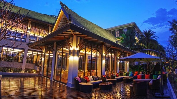 A modern hotel with a covered outdoor seating area, large windows, and a wooden deck. - Riyuegu Hotsprings Resort (Xiamen)