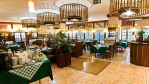 Un restaurant avec de nombreuses tables, des nappes à carreaux verts, des chaises en bois et des lampes en osier suspendues au plafond.