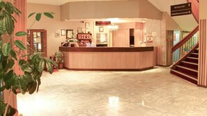Un hall d’hôtel avec un sol en marbre, un comptoir d’accueil et un escalier sur la droite.