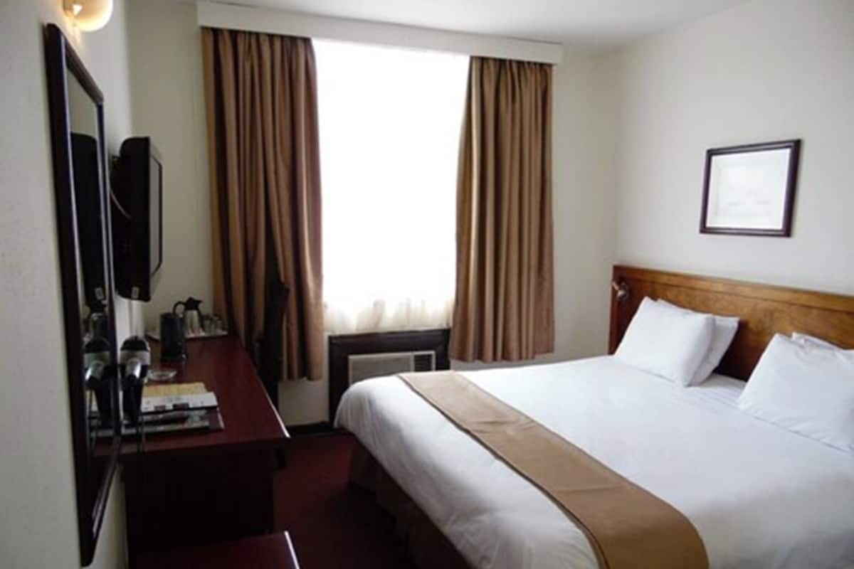 Hotelkamer met een bed, bureau, stoel, spiegel en raam met gordijnen.