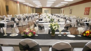 Une salle de banquet avec des rangées de tables, chacune recouverte d’une nappe noire et agrémentée de chaises blanches avec des rubans noirs.
