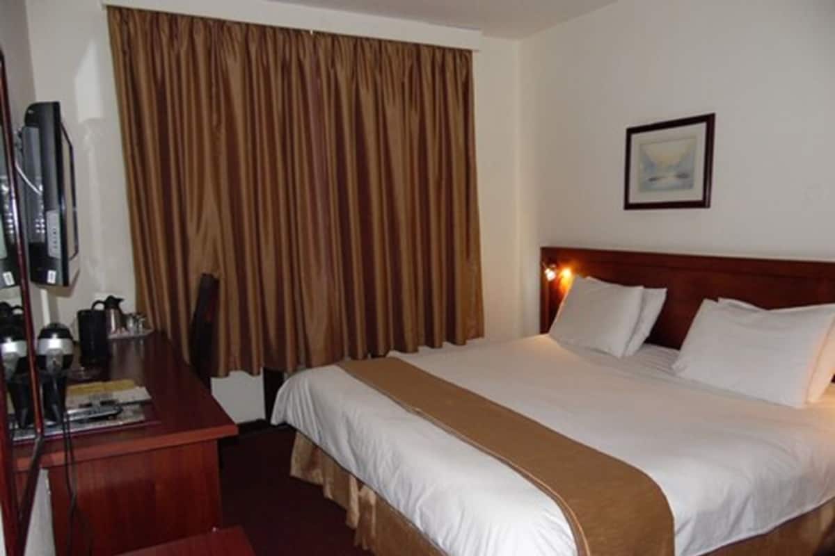 Een hotelkamer met een bed, een bureau met een televisie en een raam met gordijnen.