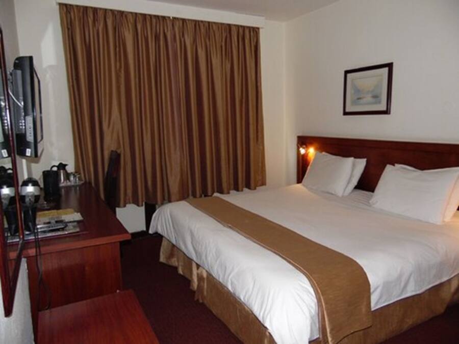 Una habitación de hotel con cama, escritorio con televisor y ventana con cortinas.
