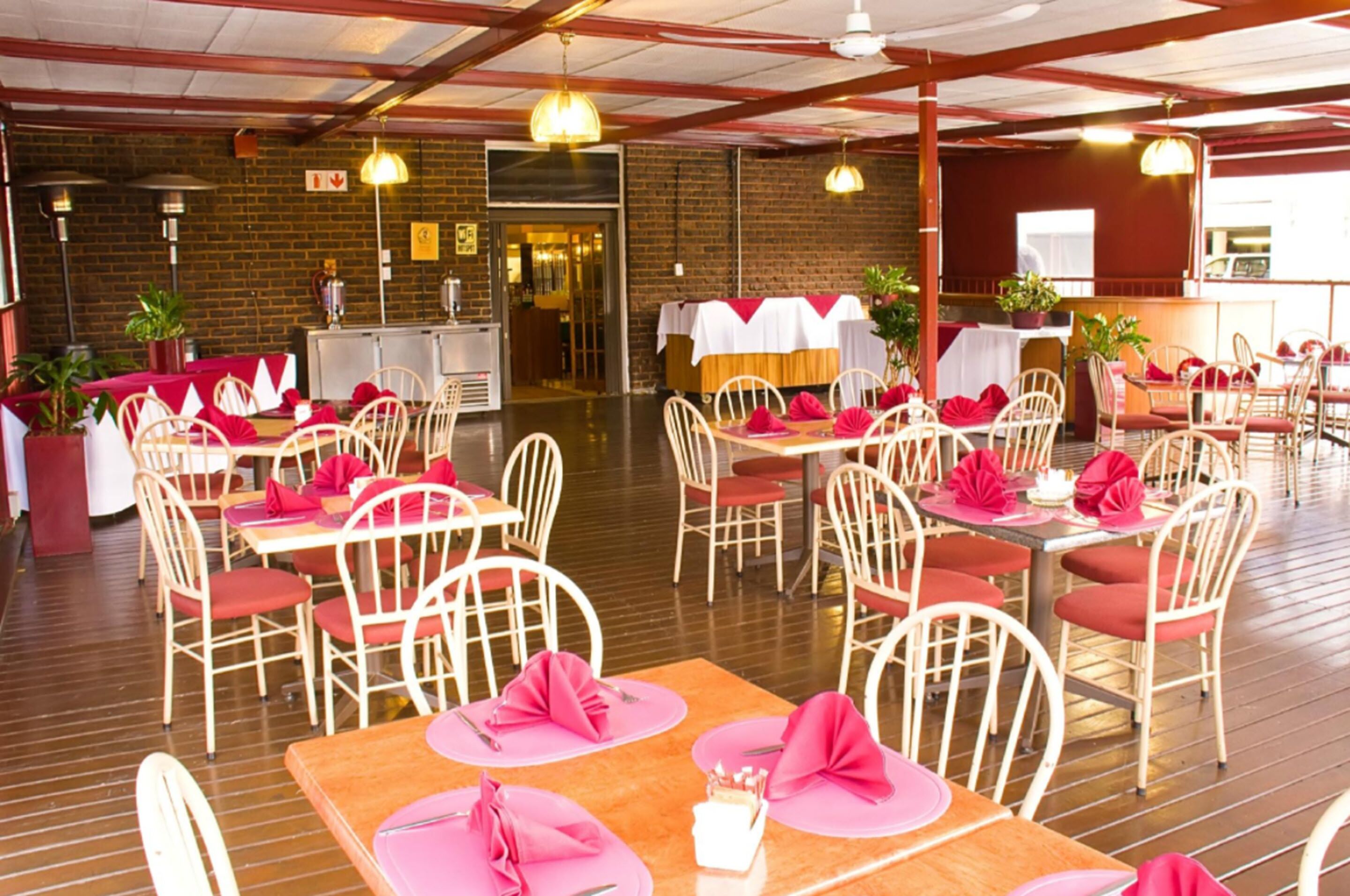 Un ristorante con pavimento in legno, sedie bianche e tavoli apparecchiati con tovaglioli rosa e cuscini rossi.