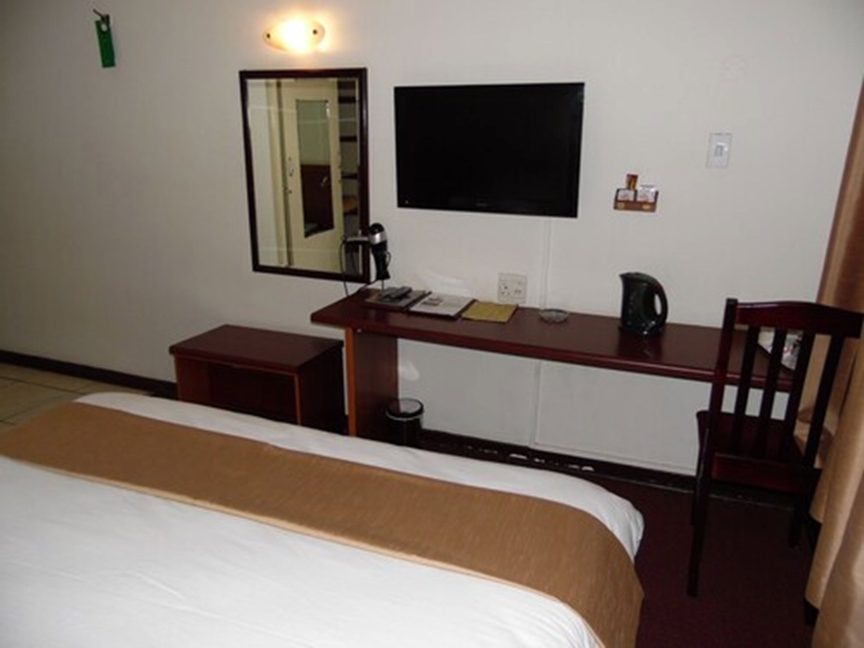 Habitación de hotel con cama, escritorio, silla, televisión y una mesita con hervidor.