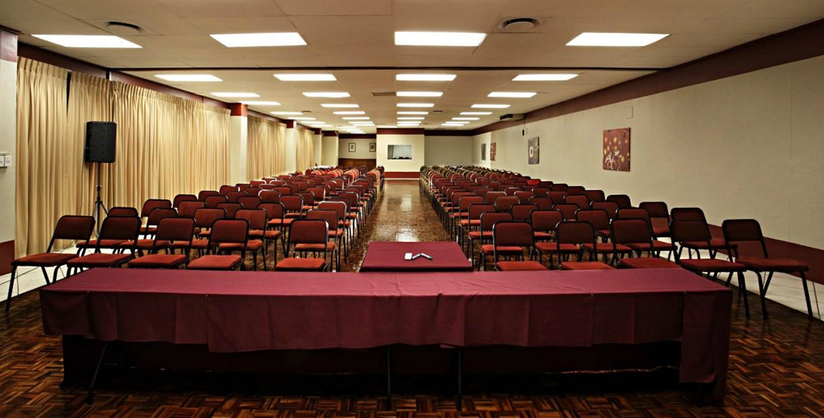 A conference room with rows of chairs and a long table, equipped with ceiling lights and a speaker.
