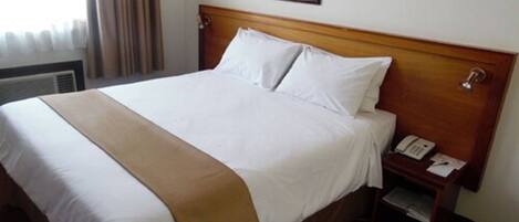 A hotel room with a wooden bed, white linens, a bedside table with a phone, and a framed picture on the wall.
