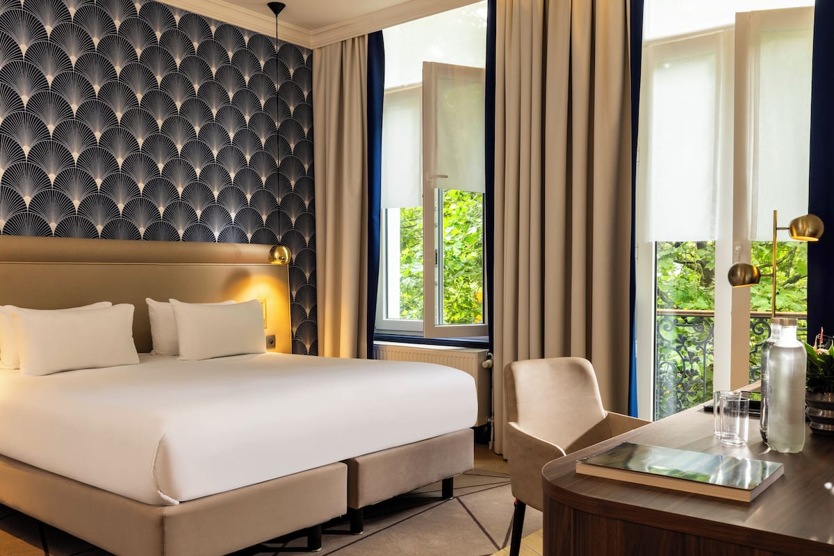 Une chambre d’hôtel avec un grand lit, une chaise, une table avec un plateau, et une vue sur la verdure à l’extérieur.