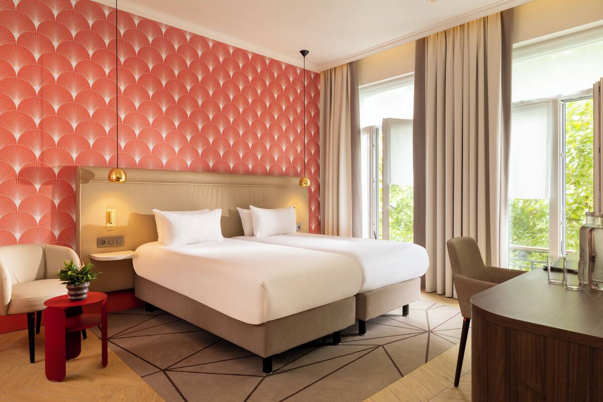 Une chambre d’hôtel moderne dotée d’un grand lit, d’un coin salon avec une table et offrant une vue sur la verdure par la fenêtre.