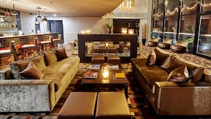 A modern lounge area with sofas, a coffee table, and a bar with bottles. - The Augustin (Brussels)