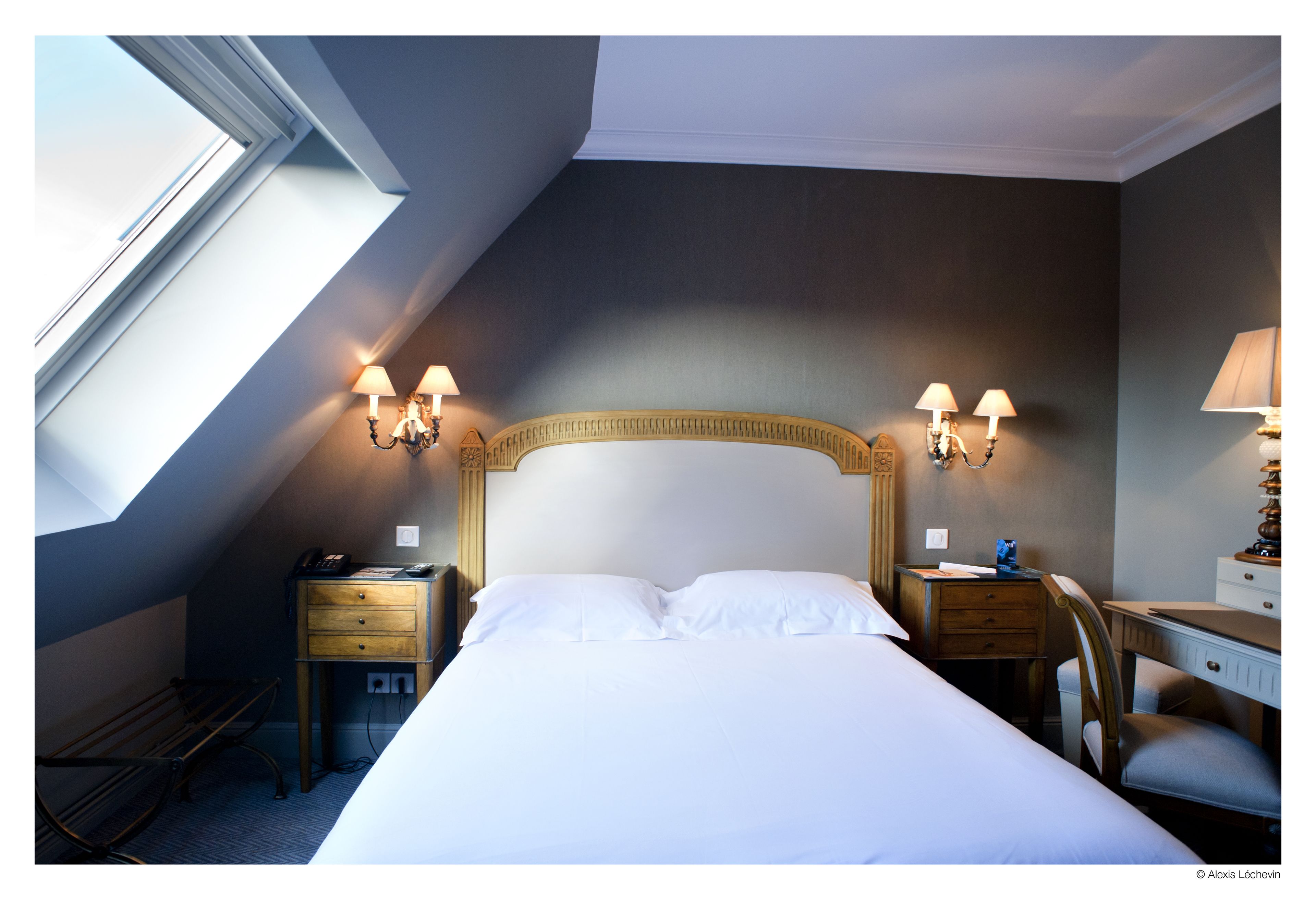 A hotel room with a large bed, a desk, two bedside tables, and a lamp.