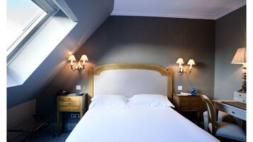 A hotel room with a large bed, a desk, two bedside tables, and a lamp.