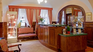 A reception area with a wooden counter, a reception desk, a seating area with a chair, and a display case with items. - Hotel Regent (Kraków)