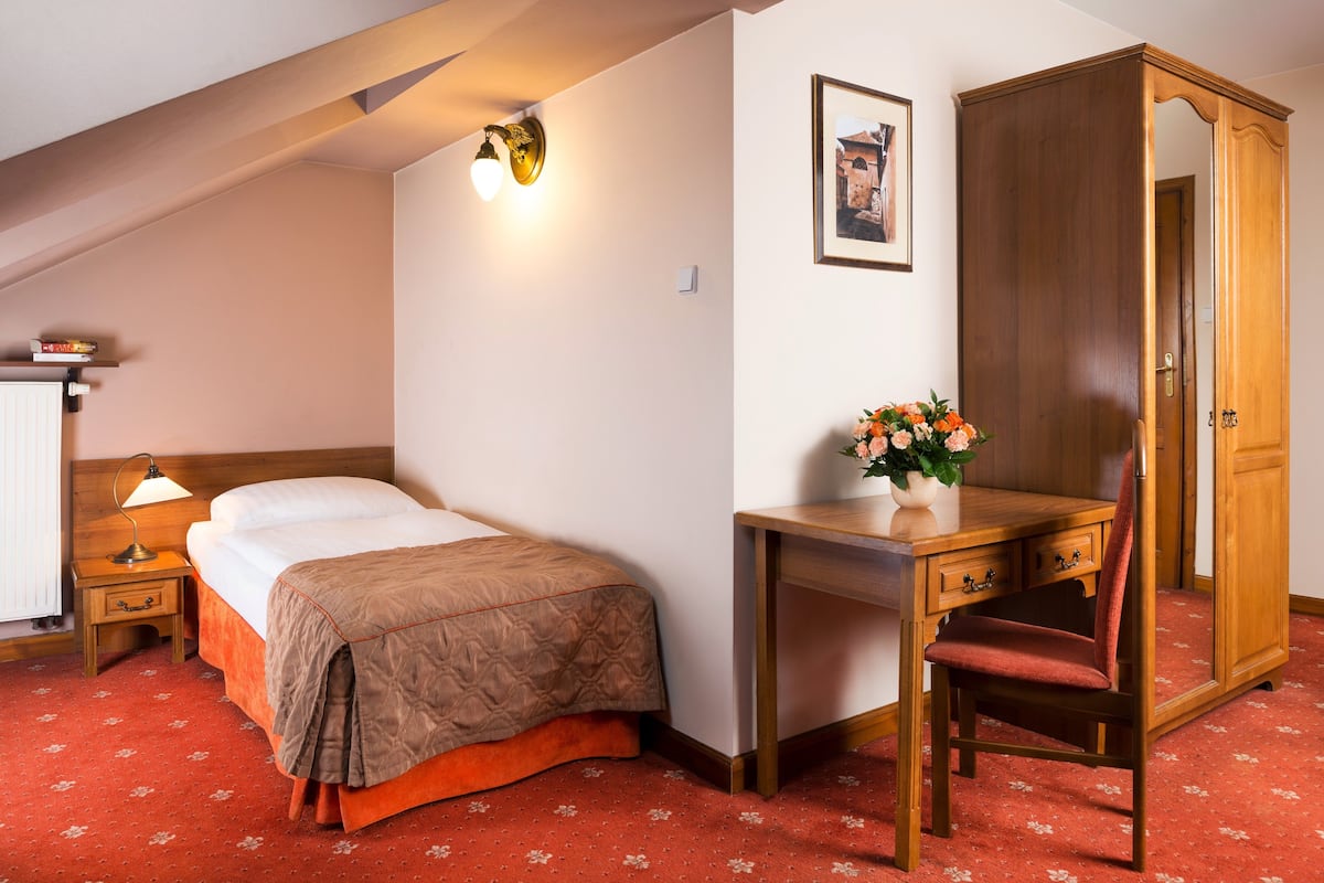 A bedroom with a bed, bedside table, lamp, desk, chair, and wardrobe.