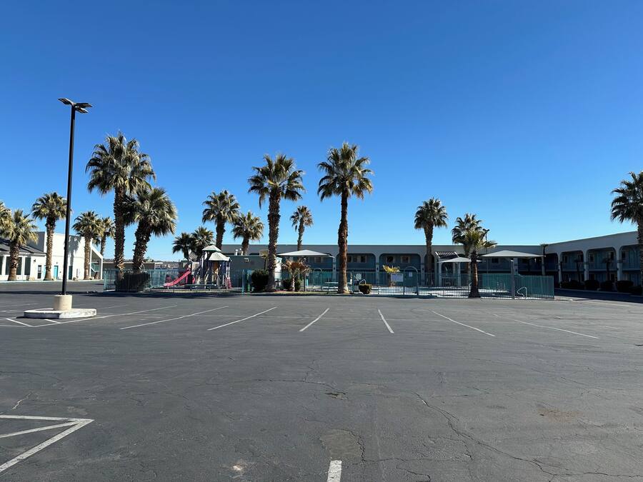 A parking lot with palm trees, a playground, and a building with a blue facade.