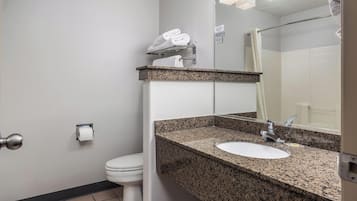 Un baño con inodoro blanco, lavamanos de encimera de granito, un espejo y un perchero para toallas.