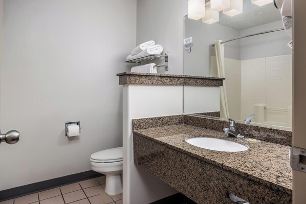 A bathroom with a white toilet, a granite countertop sink, a mirror, and a towel rack.