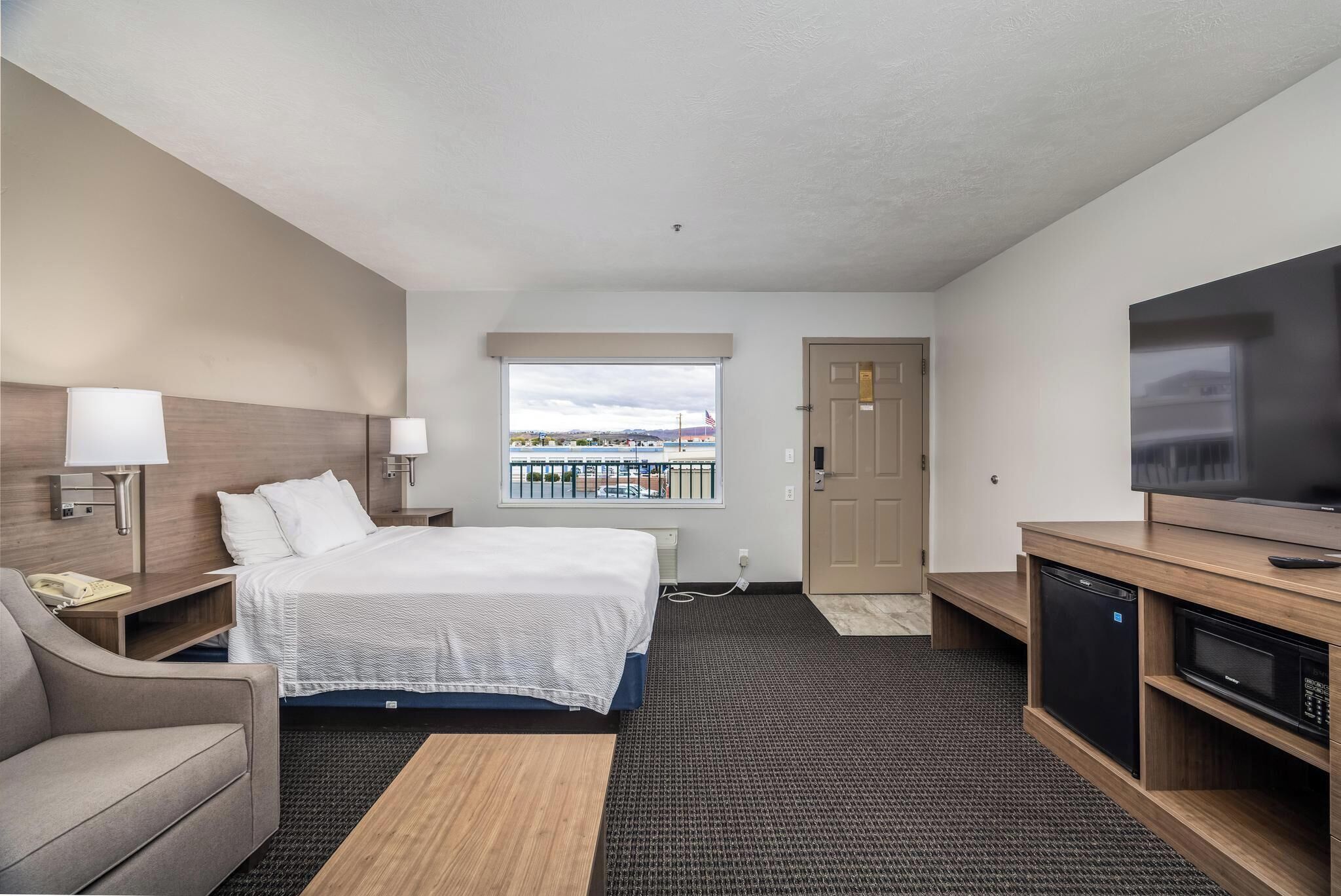 Een hotelkamer met een bed, een bureau met lamp, een televisie en uitzicht op het omliggende landschap.
