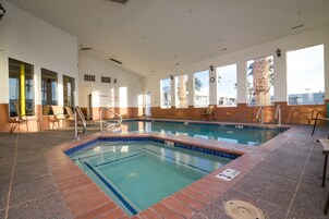 Una piscina interior con agua cristalina, bordes de azulejos y una zona de solárium con baldosas.