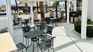 An outdoor patio with tables and chairs, a white pergola, and palm trees. - St. George Inn & Suites (St. George)