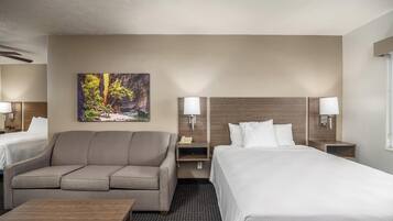 A hotel room with a bed, a sofa, a desk, and a painting of a forest scene.