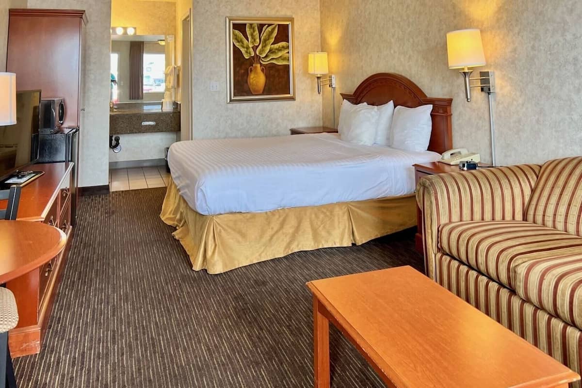 A hotel room with a bed, a sofa, a desk, a lamp, and a painting on the wall.
